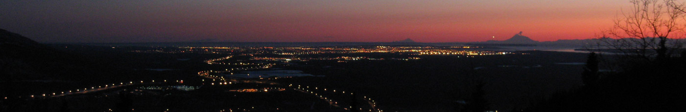 When Redoubt volcano began to emit steam and a little ash in early March, I photographed it at sunset from the road on the south side of Mount Baldy in Eagle River. That's Anchorage spread out in the middle distance. The bright light in the sky next to Redoubt is a plane landing at the Anchorage International Airport. The next cone-shaped mountain down the coast is Iliamna. Photo copyright 2009 by Leon Unruh.